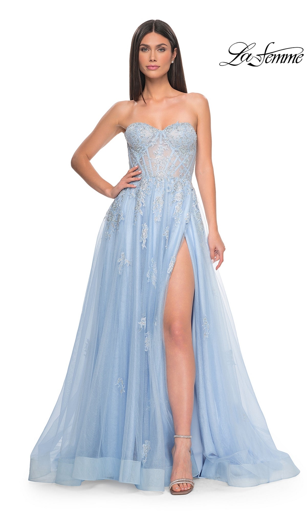 A woman in the La Femme Strapless Long A-Line Prom Dress 32111, light blue with embroidered lace appliques, a high slit, and tulle overlay, poses against a white background.